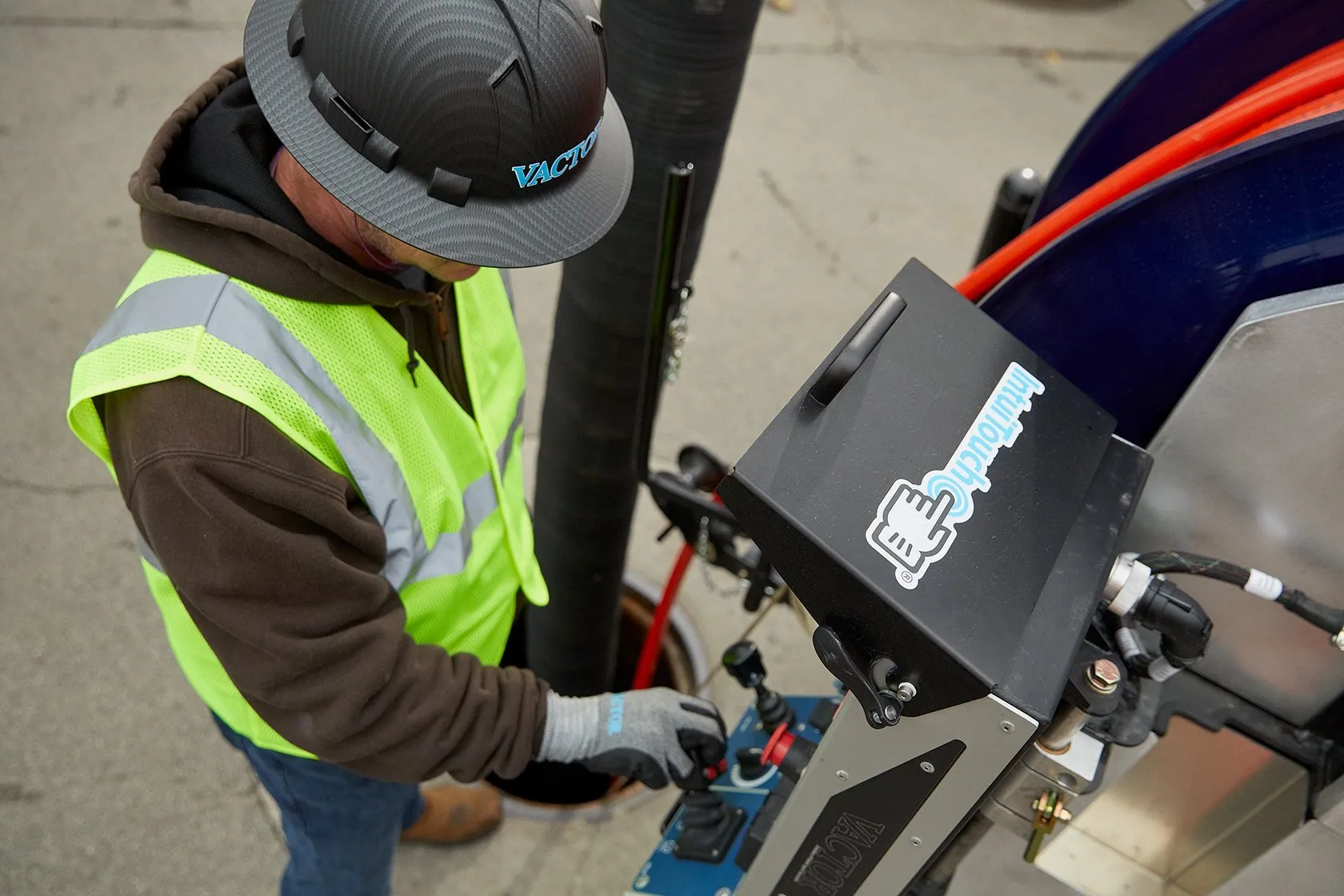 A construction worker in a safety vest and hard hat operates a control panel on industrial pipe-laying equipment.