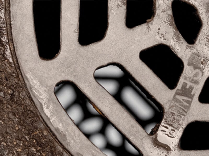 Close-up of a rusty, textured metal manhole cover with visible grates and embossed text.